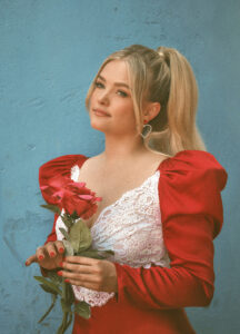 Photo of Jailey Whitters in a white dress with red sleeves, she is holding red flowers