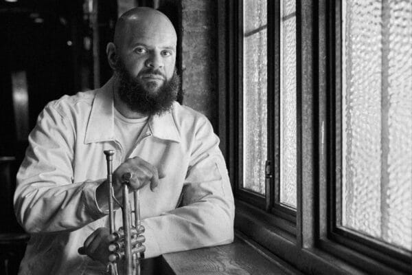 Black and white photo of Dave Guy holding a trumpet near a window.