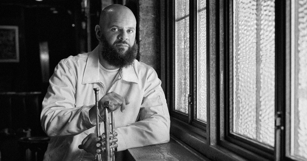 Black and white photo of Dave Guy holding a trumpet near a window.