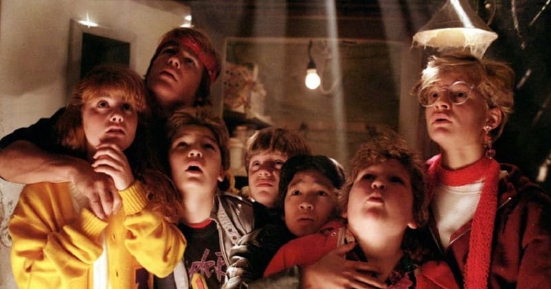 Group of seven main cast members in the Goonies looking up through floor slats