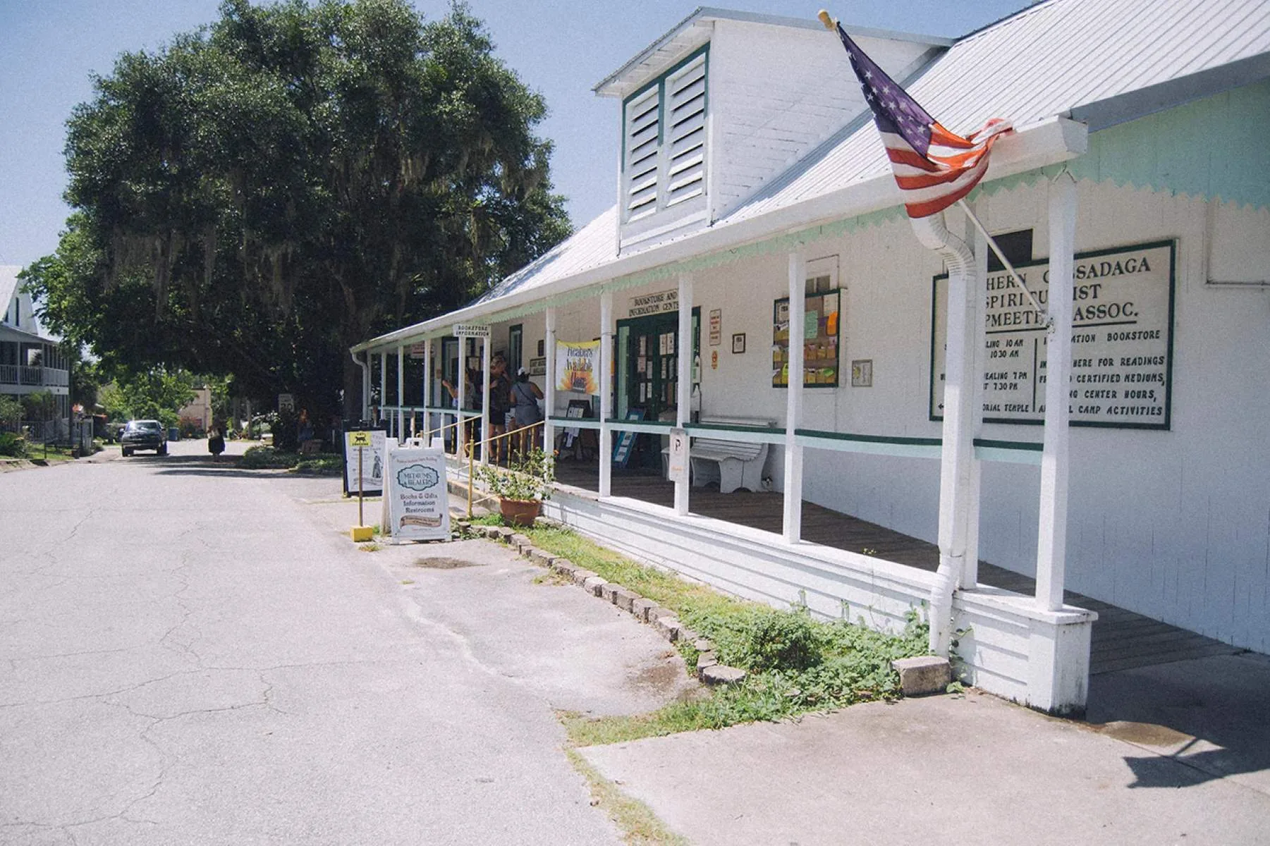 A photograph of the Southern Cassadaga Spiritualist Camp sign, featuring the iconic sunflower emblem and the inscription "Camp Closed from Dusk Till Dawn."