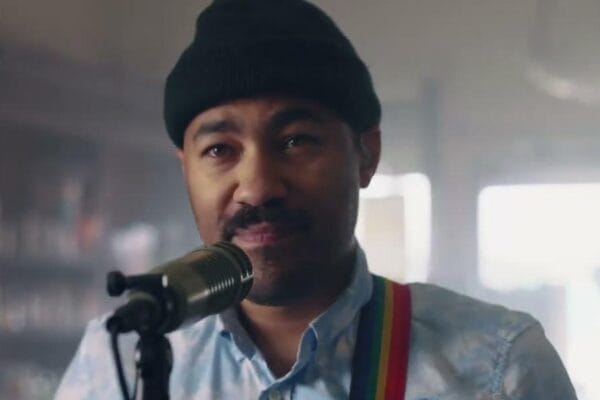 San Gabriel Chronicles a Bold Debut with Nights and Weekends San Gabriel closeup wearing black beanie standing at microphone with visible rainbow stripe guitar strap