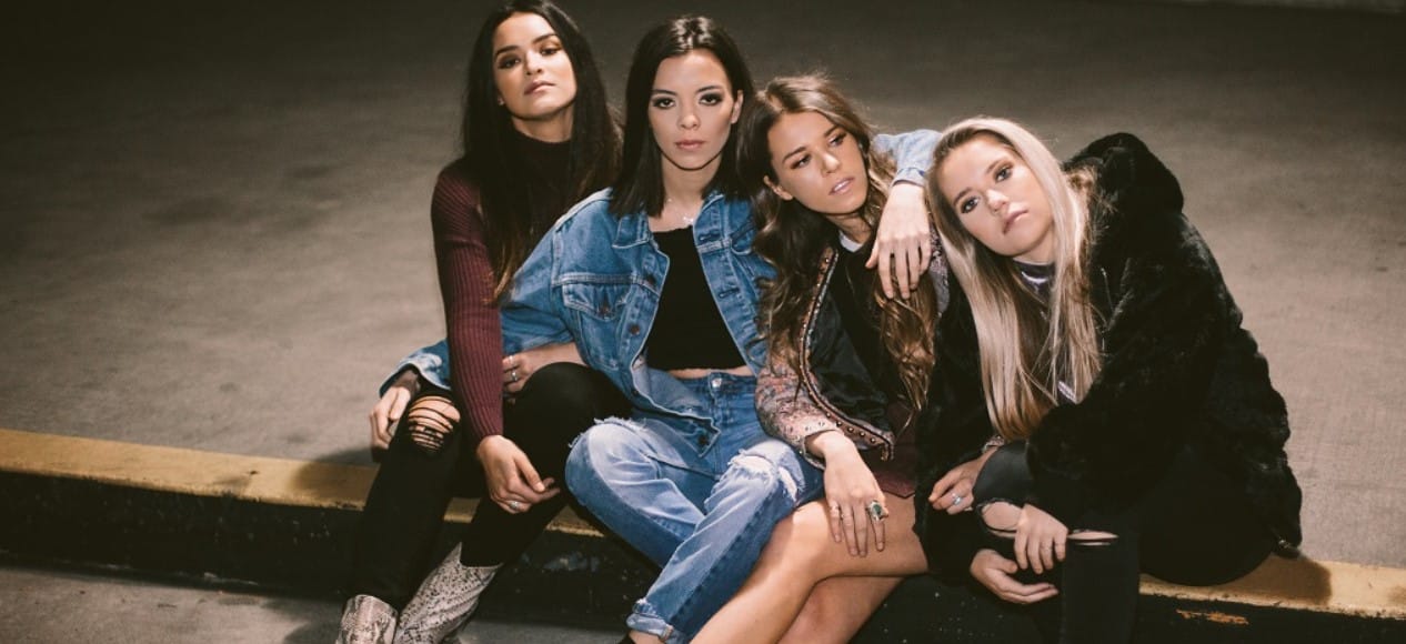 Group shot of the Aces band sitting on a curb, four women