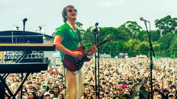 Joe Keery wearing green short sleeve shirt and sunglasses holding guitar and singing