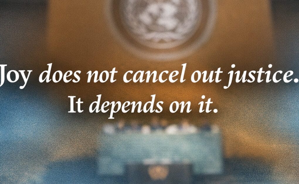 Blurred view of the United Nations General Assembly chamber with white text reading, “Joy does not cancel out justice. It depends on it.”